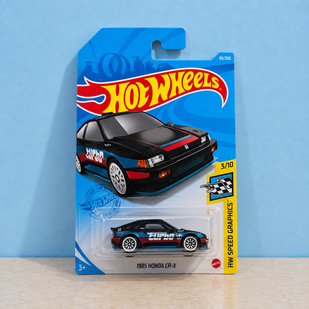 A Hot Wheels die-cast toy car in its original blister card packaging, featuring a 1985 Honda CR-X with blue, red, and black livery. The card is branded with the classic Hot Wheels logo and shows a blue background.